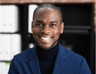 A person in a blue blazer smiles in front of shelves with binders.